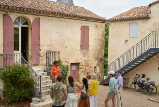 Visitors gathered in the courtyard of Château Tour Baladoz in Bordeaux, featuring stone buildings, tiled roofs, and a conical tower in the background.
