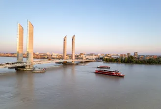 The Lifting Bridge of Pierre d'Espagne in Bordeaux with two red tourist boats navigating the Garonne River at sunset