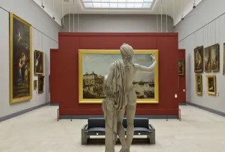 Gallery of the Bordeaux Museum of Fine Arts featuring a marble statue in the foreground facing gilt-framed historical paintings on white and burgundy walls, with overhead lighting.