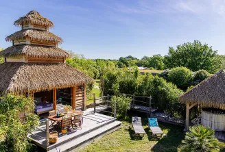 Aerial view of an eco-tourism resort featuring thatched-roof bungalows, wooden decks, pool, and lush green surroundings near Bordeaux