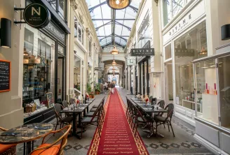 Elegant covered arcade in Bordeaux with luxury shops, restaurant tables, glass ceiling and red carpet on the floor