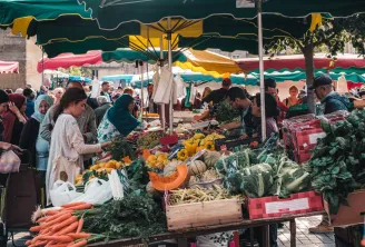 Open-air market in Bordeaux with fresh produce stalls under green and yellow awnings, shoppers browsing between vendors' stands