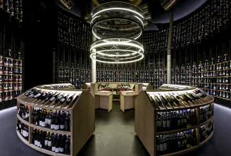 Modern wine cellar of Latitude 20 Wine Bar in Bordeaux, featuring curved shelves filled with wine bottles, a central wooden counter, and circular white ceiling lighting.