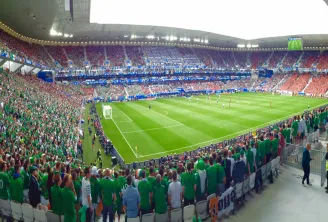 Interior view of Stade Atlantique Bordeaux Métropole filled with supporters wearing green and red jerseys during a football match, with the green pitch and crowded stands.