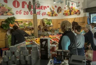 Interior of the Chartrons covered market in Bordeaux with customers shopping at a fresh produce stall, wall display with fruits and phone number