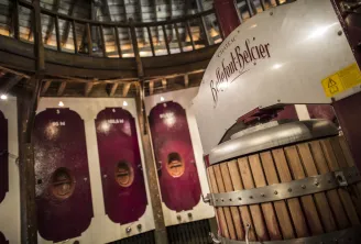 Interior of Château Bellefont-Belcier in Bordeaux displaying wooden fermentation vats with metal bands and a large white vat bearing the château's name, beneath a circular architectural structure.