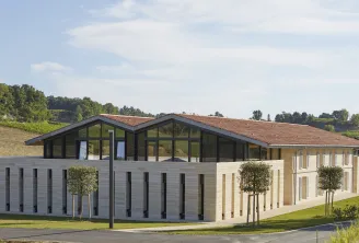 Château Peby Faugères in Bordeaux: modern architectural building with white and grey facades, red tile roof, large glass panels and black shutters, surrounded by landscaped gardens and vineyards.