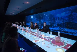 Futuristic dining room with interactive illuminated table, panoramic nighttime view with moon and trees on giant screen, diners seated on both sides