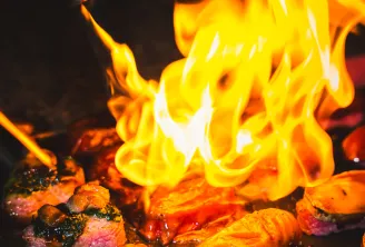 Bright yellow and orange flames rising above glowing embers and hot coals in a fire pit