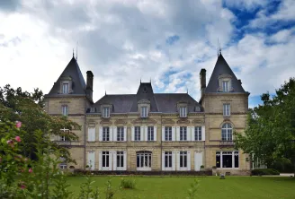 Front facade of the National Health Insurance Museum in Bordeaux, a Second Empire-style château with two pointed towers, surrounded by green lawns and pink flowers.