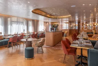Elegant restaurant at Madame B in Bordeaux featuring red chairs, round tables, glossy white ceiling, large bay windows, and light wood modern furniture