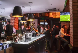 Lively interior of Bodega Bodega bar in Bordeaux with patrons at the counter, black pendant lights, exposed brick walls, and football match on screen