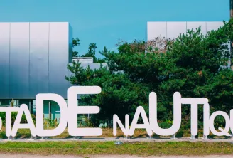 White letter sign reading « STADE NAUTIQUE » in front of a modern building with blue and white facades and lush green vegetation in Bordeaux.