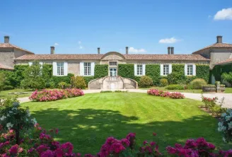 Front view of an elegant Bordeaux mansion at Chambres d'Arche featuring white façade, tiled roof, lush green lawn and vibrant pink and magenta flower beds