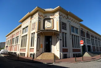 Facade of Les Bains municipal swimming pool in Bordeaux, Art Deco building with geometric brick and white stone details, central entrance with clock.
