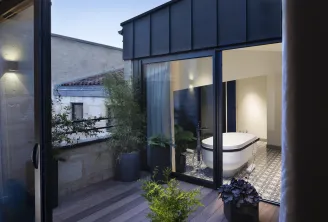 Outdoor terrace featuring a luxurious white bathtub, overlooking the courtyard of Hôtel Cardinal in Bordeaux, with evening lighting and decorative plants.