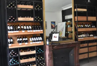Interior of a Bordeaux wine shop featuring wooden shelves displaying wine bottles, an ornate wooden counter with a gilded mirror, and storage display cases.