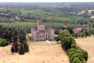 Aerial view of Château de Roquetaillade with its crenellated towers surrounded by fields and lush forests in Aquitaine.