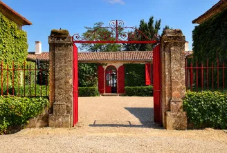 Red entrance gate of Château Sigalas Rabaud in Bordeaux, framed by stone columns with manicured gardens and ivy, leading to a paved courtyard