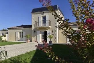 Modern neoclassical villa with white facade, square tower, wrought iron balcony, black slate roof, columned entrance, gravel driveway and landscaped gardens in Bordeaux