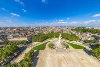 Aerial view of the Esplanade des Quinconces in Bordeaux featuring the Girondins Monument in the center, surrounded by gardens and trees, overlooking Haussmann-style buildings