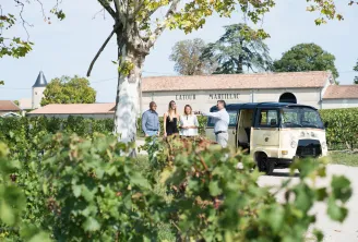 Guided tour at Château Latour-Martillac in Bordeaux with visitors gathered near a vintage tour vehicle, surrounded by vineyards and the historic winery building.