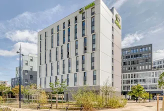 Facade of B&B Hotel Bordeaux Centre Gare Saint-Jean, a modern white multi-story building with green signage, located in a public square with trees and benches