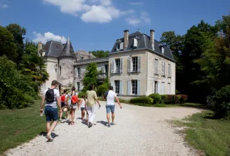 Group of visitors walking on a gravel path in front of Château Bardins, a 19th-century mansion with turrets and mansard roofs, surrounded by greenery near Bordeaux.
