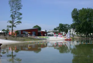 Bègles Beach in Bordeaux featuring a red building by the water, colorful sailboats, trees, and a person in the foreground