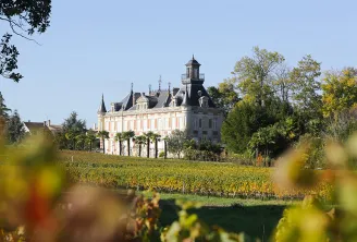Marquis d'Alesme Becker Castle, a grand Bordeaux-style château with towers and mansard roof, surrounded by autumn vineyards in the Bordeaux wine region.