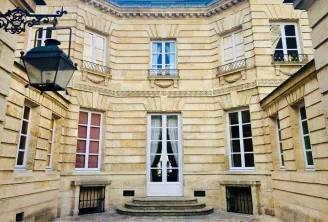 Interior courtyard of the small Labottière mansion in Bordeaux, featuring symmetrical ashlar stone facade, evenly spaced windows, central entrance door, and ornamental wall lantern.