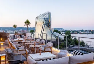 Panoramic terrace of Renaissance Bordeaux Hotel featuring contemporary furniture, overlooking the Garonne River and modern glass and steel building architecture at dusk