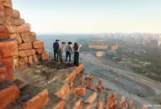 Four people standing on a red rocky cliff overlooking the panoramic view of Bordeaux city, river, and buildings in golden light.