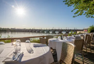 Restaurant terrace overlooking the Garonne River in Bordeaux with set tables, view of the Stone Bridge and city skyline on a sunny day
