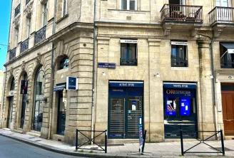 Haussmannian building facade in Bordeaux with ground floor shops, including a jewelry store OR EXPERTISE and a currency exchange office, on Jean-Jaurès street.