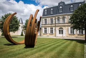 Abstract rust-colored metal sculpture in front of Château Malescasse in Bordeaux, featuring the castle's distinctive stone facade and mansard roof.