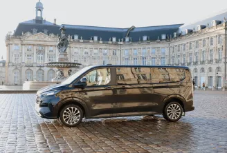 A black minivan parked on Place de la Bourse in Bordeaux, facing the historic 18th-century buildings and central equestrian statue