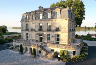Château Grattequina in Bordeaux, a 19th-century stone mansion with mansard roofs overlooking the Garonne river, featuring ornamental terraces and wrought-iron balconies.