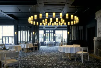 Elegant dining room at La Grand'Vigne in Bordeaux featuring round tables with white linens, modern brass chandelier, floor-to-ceiling windows, and contemporary minimalist decor.