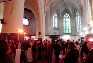Crowd of visitors inside Espace Saint Rémi in Bordeaux, a Gothic church converted into an exhibition space with ribbed vaults, stained glass windows and pink columns.