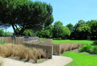 Public park along the Jalle de Gajac waterfront in Bordeaux featuring green lawns, ornamental grasses, wooden and metal fencing, mature trees and clear sky