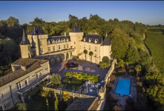 Aerial view of Château de La Rivière near Bordeaux, featuring Renaissance architecture with conical towers, paved courtyard, swimming pool, and surrounding vineyards.