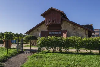 Modern building of the Wine and Vineyard Ecomuseum in Gradignan, featuring stone facade and wooden roof, surrounded by vineyards and fencing, with clear blue sky.