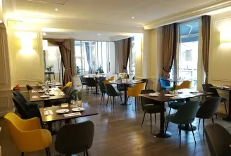 Elegant dining room at Comptoir de Sèze in Bordeaux featuring black tables, yellow and blue chairs, large windows, beige and gold decor, with an outdoor terrace view.