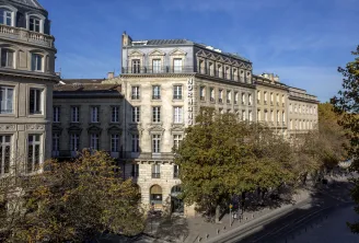 Facade of the Hôtel de Normandie in Bordeaux, a historic Haussmann-style building featuring mansard roofs and architectural ornaments, surrounded by autumn foliage.