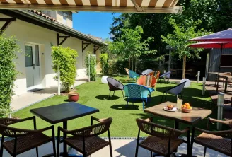 Sunny hotel terrace with colorful seating, dining tables, loungers, green lawn, umbrellas and white building in the background in Bordeaux