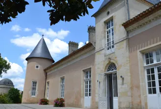Facade of Château Lescombes, a contemporary art center in Bordeaux, featuring its distinctive round tower, white windows, and beige stone walls under a blue sky.