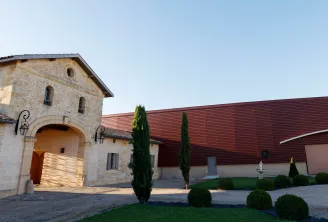 Château du Lort in Bordeaux: stone facade with arched gateway and red roof, surrounded by cypress trees and landscaped garden