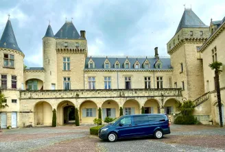 Château de la Malromé in Bordeaux featuring pointed turrets, stone facade, vaulted arcades and a blue minivan parked in the brick courtyard