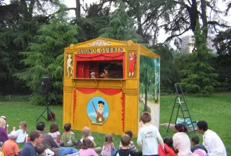 Guignol Guérin puppet theater in Bordeaux, a yellow and red wooden structure with children seated on grass in a park watching the show.